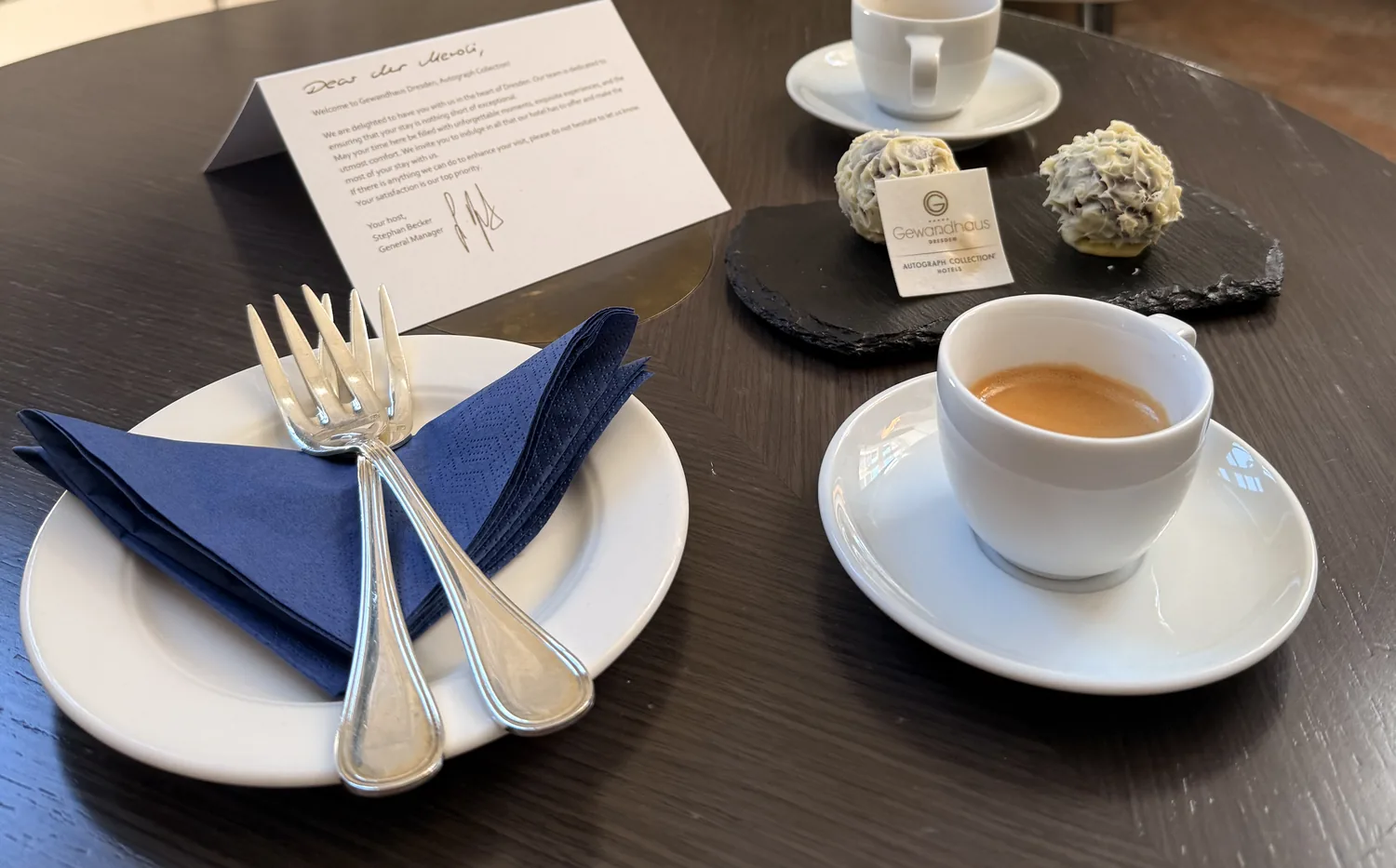 Two white-chocolate pralines, two forks and two espressos set out as a welcome in a Dresden hotel room